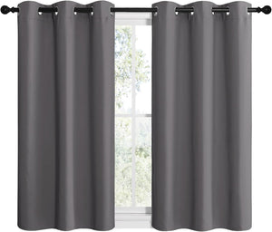 Pair of dark gray grommet top curtains on a black rod, covering a window with trees outside.