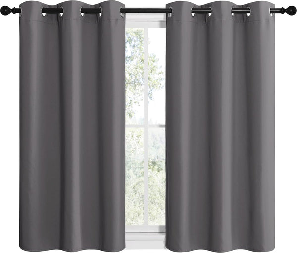 Pair of dark gray grommet top curtains on a black rod, covering a window with trees outside.