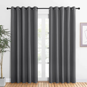 Two dark gray blackout curtains with grommet tops hanging on a black rod over a bright window.