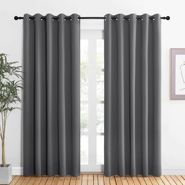 Two dark gray blackout curtains with grommet tops hanging on a black rod over a bright window.