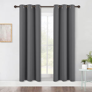 Two dark gray blackout curtains with silver grommet tops hanging on a bronze rod over a window.