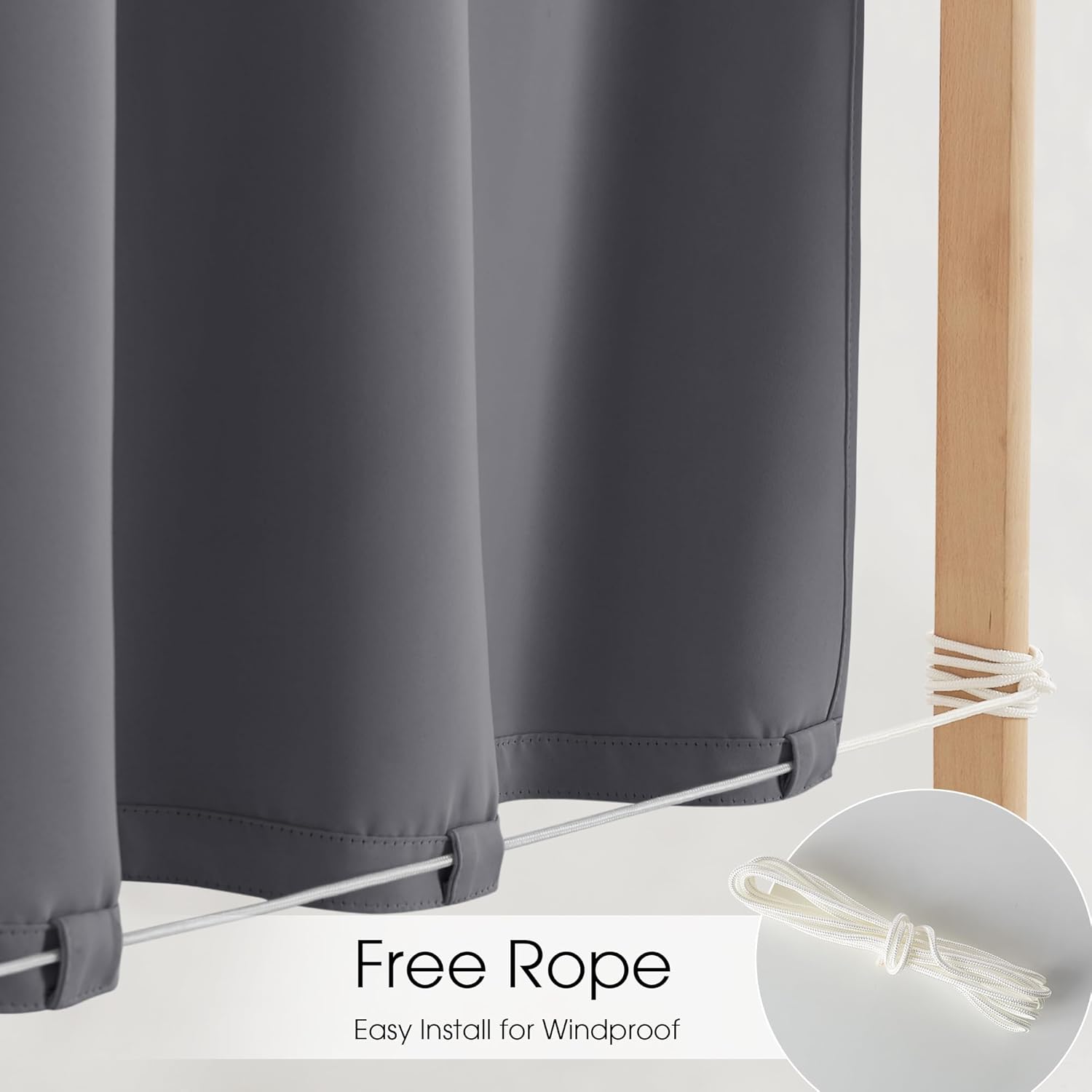 Dark gray outdoor curtain with white rope through bottom loops, tied to wooden post for windproof.