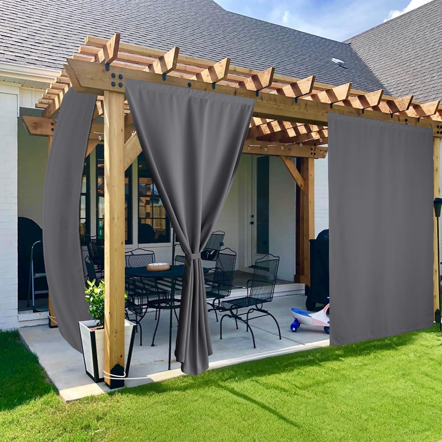 Dark gray outdoor curtains on a wooden pergola patio, one tied back, offering shade and privacy.