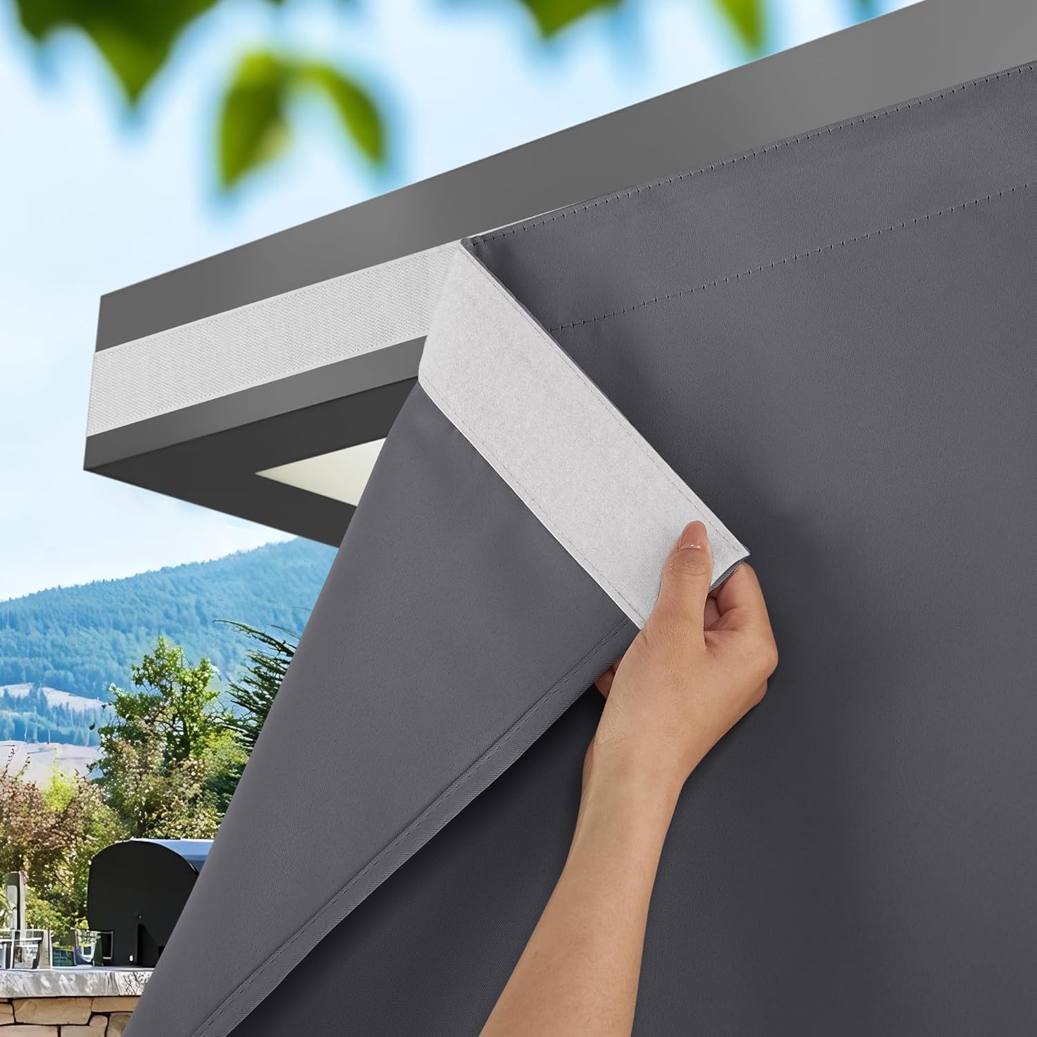 Hand attaching dark gray outdoor privacy screen to a pergola using hook-and-loop fasteners.