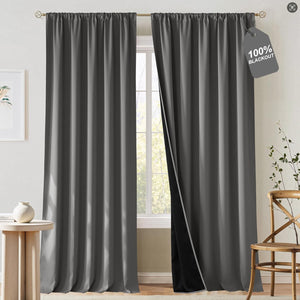 Dark gray rod pocket blackout curtains hanging on a gold rod, one panel revealing a black lining for light blocking.