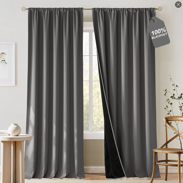 Dark gray rod pocket blackout curtains hanging on a gold rod, one panel revealing a black lining for light blocking.