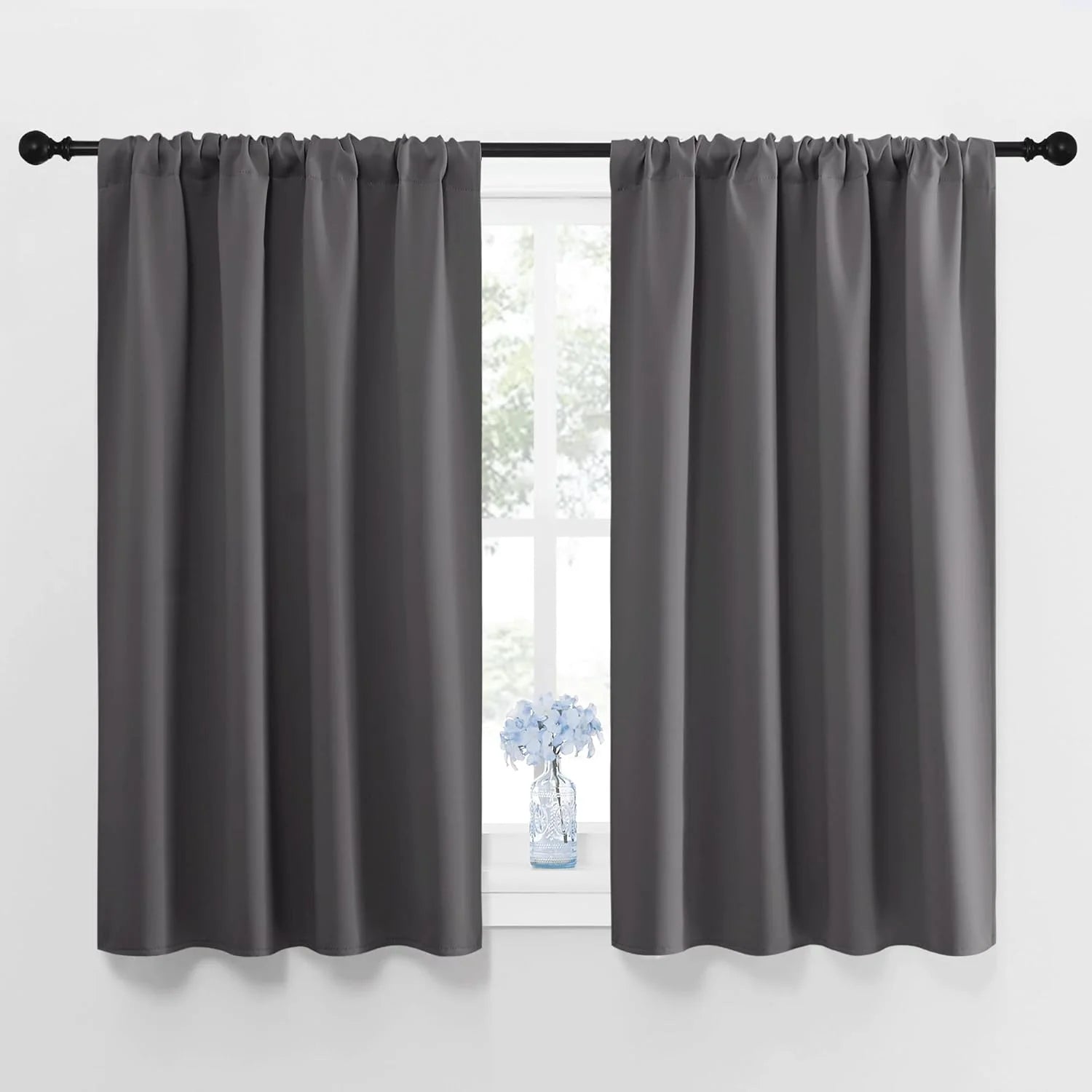Pair of dark gray rod pocket tier curtains covering a window, with a black rod and small vase.