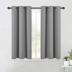 A pair of dark gray room darkening curtains with silver grommet tops hung on a decorative brown rod above a window.