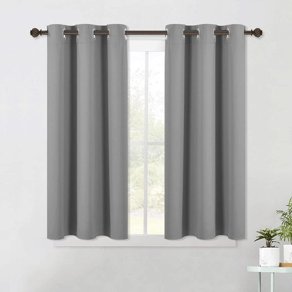 A pair of dark gray room darkening curtains with silver grommet tops hung on a decorative brown rod above a window.