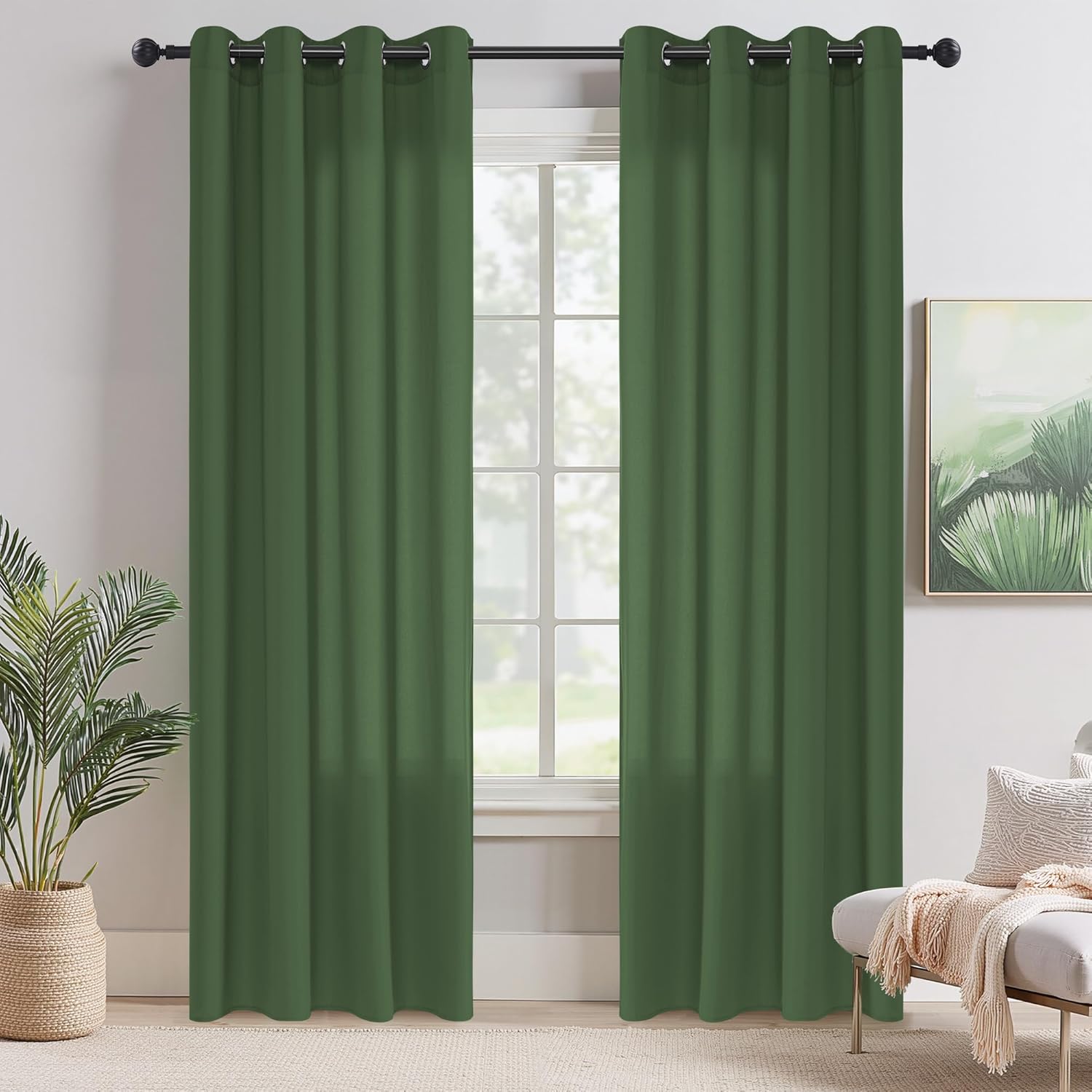 Pair of dark green blackout curtains with grommet tops hanging on a black rod in a bright room.