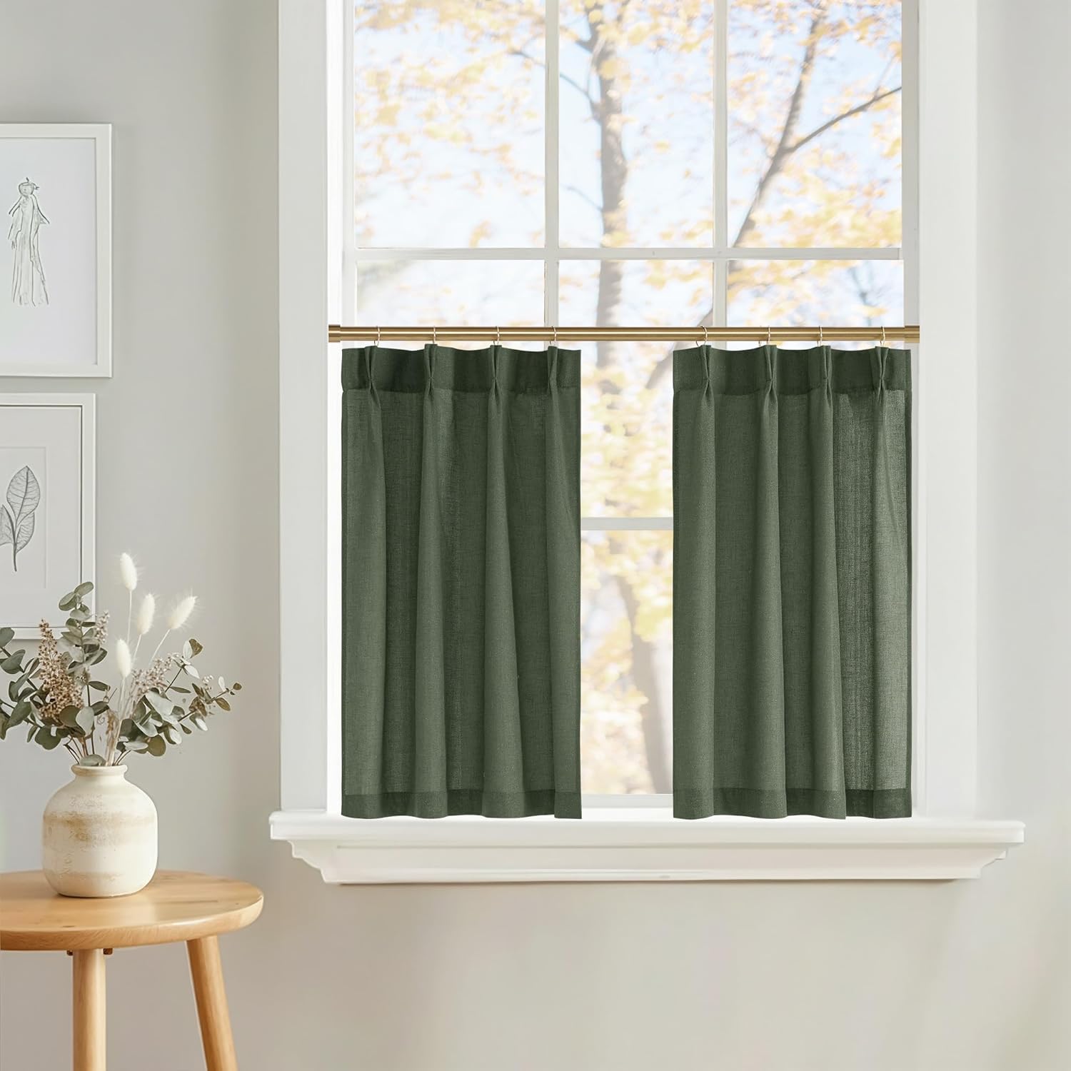 Textured dark green cafe curtains with tailored pleats hanging from a brass rod over a sunlit window.