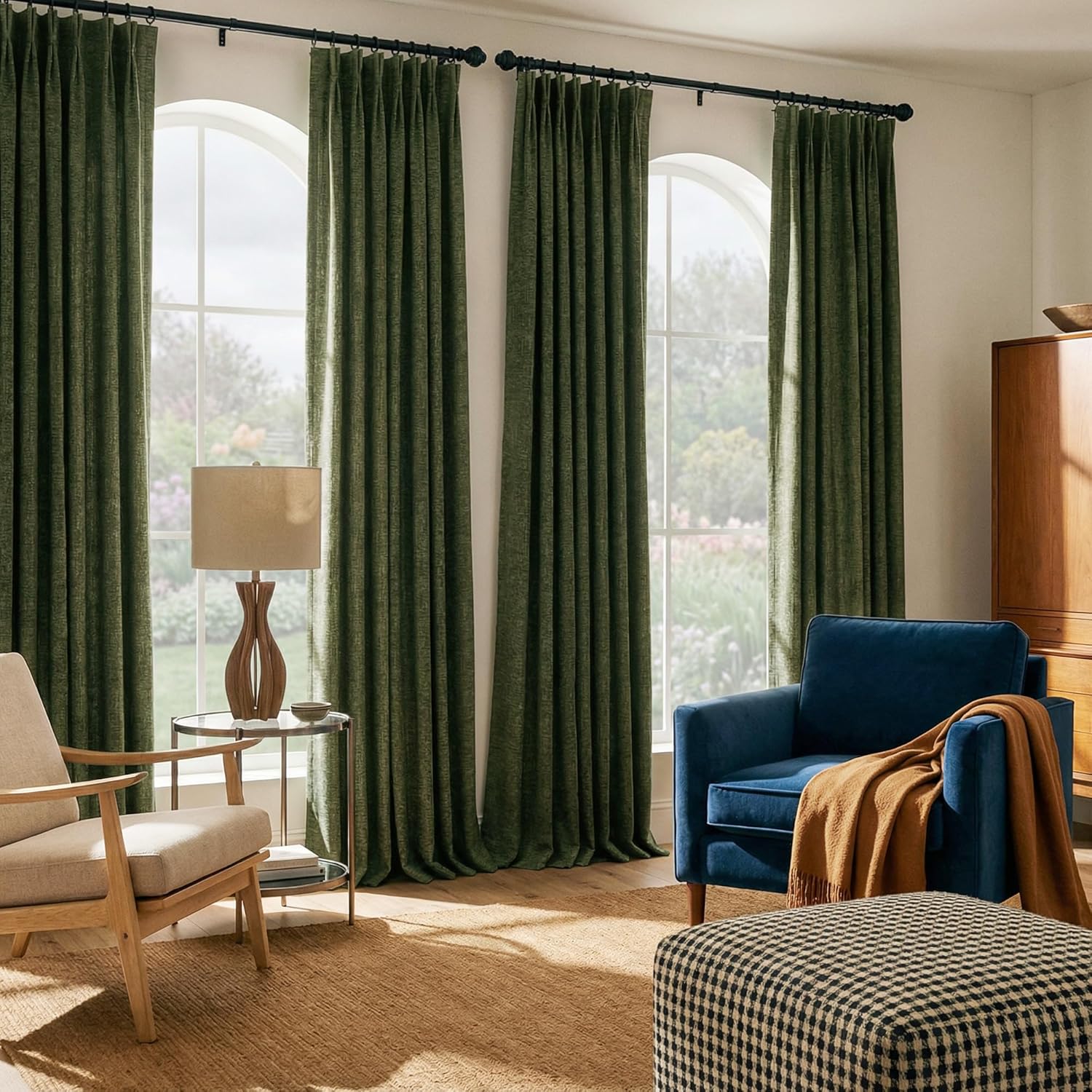 Dark green textured pleated curtains on black rods, covering arched windows in a sunlit living room.