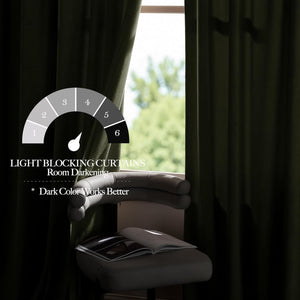 Dark green velvet light blocking curtains drawn across a window, providing strong room darkening, next to a chair with a book.