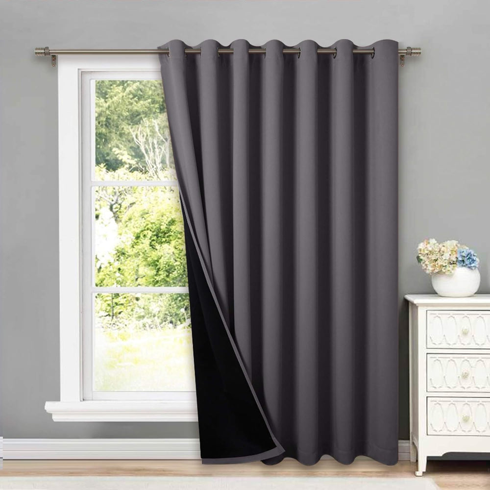 Dark grey blackout grommet curtain panel hanging on a window with a metal rod, revealing its black lining.