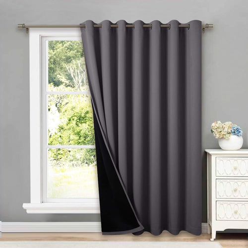 Dark grey blackout grommet curtain panel hanging on a window with a metal rod, revealing its black lining.