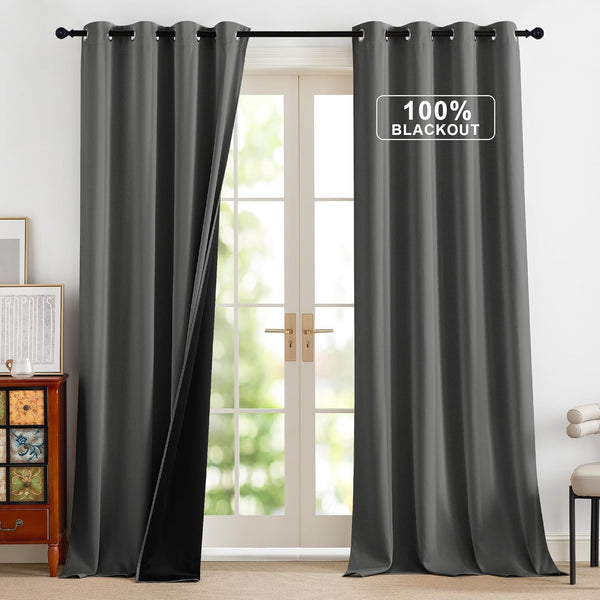 Dark grey 100% blackout curtains with grommet tops hanging by a glass door. Thick fabric blocks light.