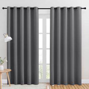 Two panels of dark grey blackout curtains with black grommet tops, hanging on a black rod over a bright window.