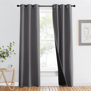 Dark grey blackout curtains with silver grommet tops hanging on a black rod in a modern room.