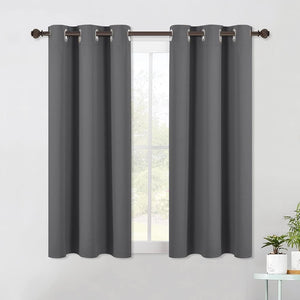 Two dark grey blackout curtains with silver grommets hanging on a bronze rod over a window.