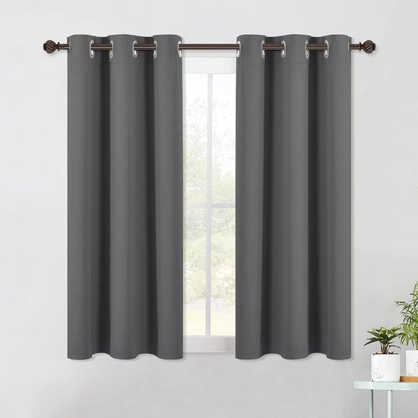 Two dark grey blackout curtains with silver grommets hanging on a bronze rod over a window.