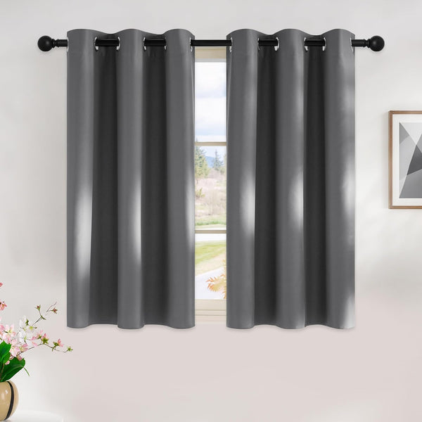 Two dark grey blackout curtains with silver grommet tops hanging on a black rod over a window.