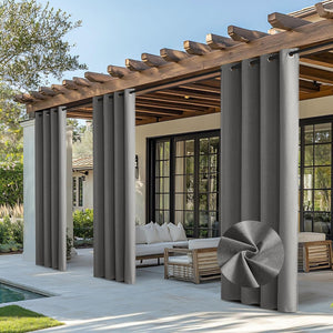 Dark grey outdoor grommet curtains hang on a wooden pergola, shading a patio. Woven fabric texture visible.