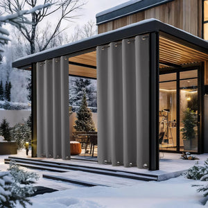 Dark grey grommet top outdoor curtains hang on a modern patio pergola in a snowy winter landscape.