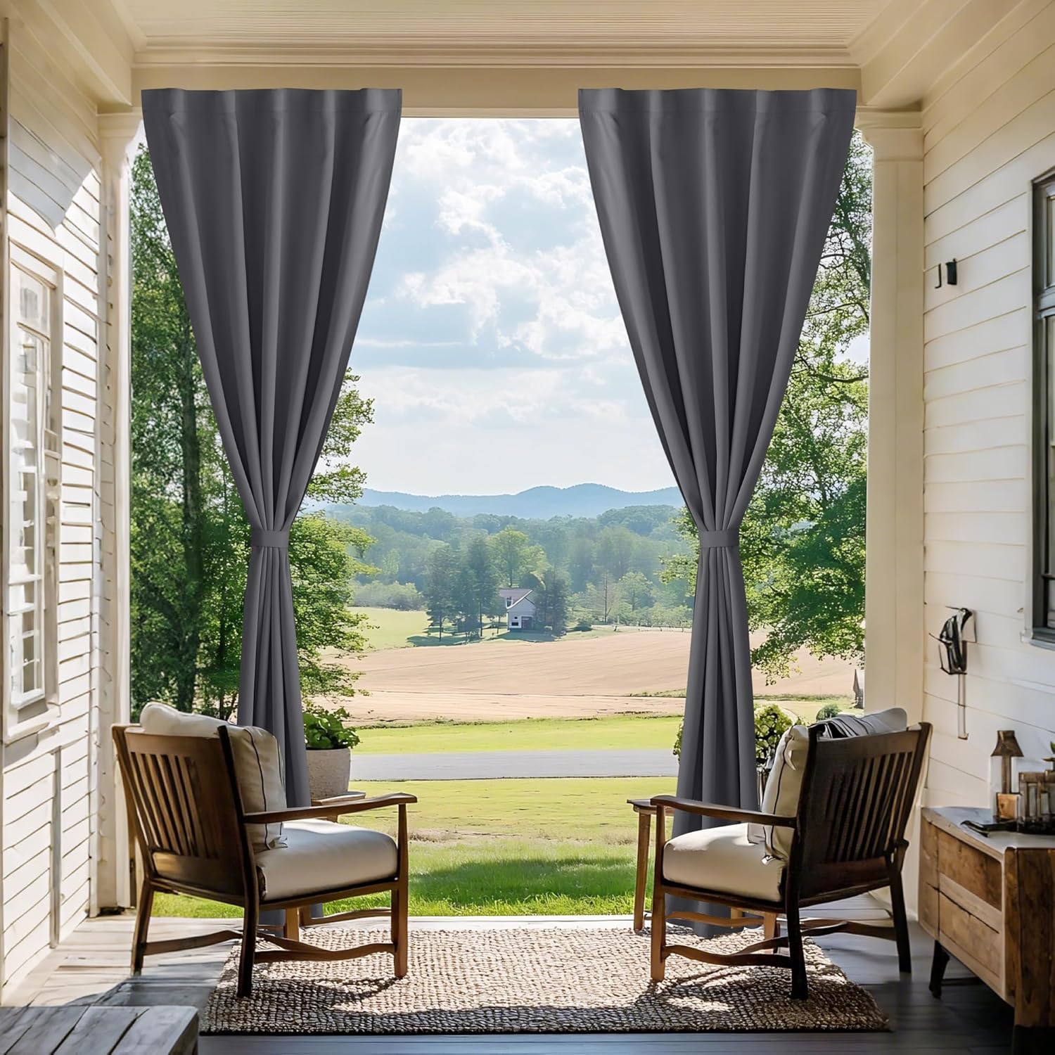 Dark grey outdoor patio curtains with grommet tops, tied back on a porch, overlooking a scenic valley.