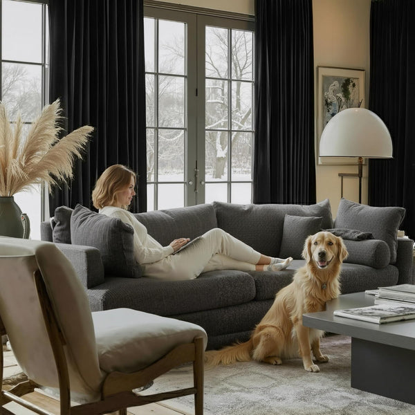 Dark grey textured modern sectional sofa in a bright living room. A woman relaxes on it, golden retriever sits nearby.