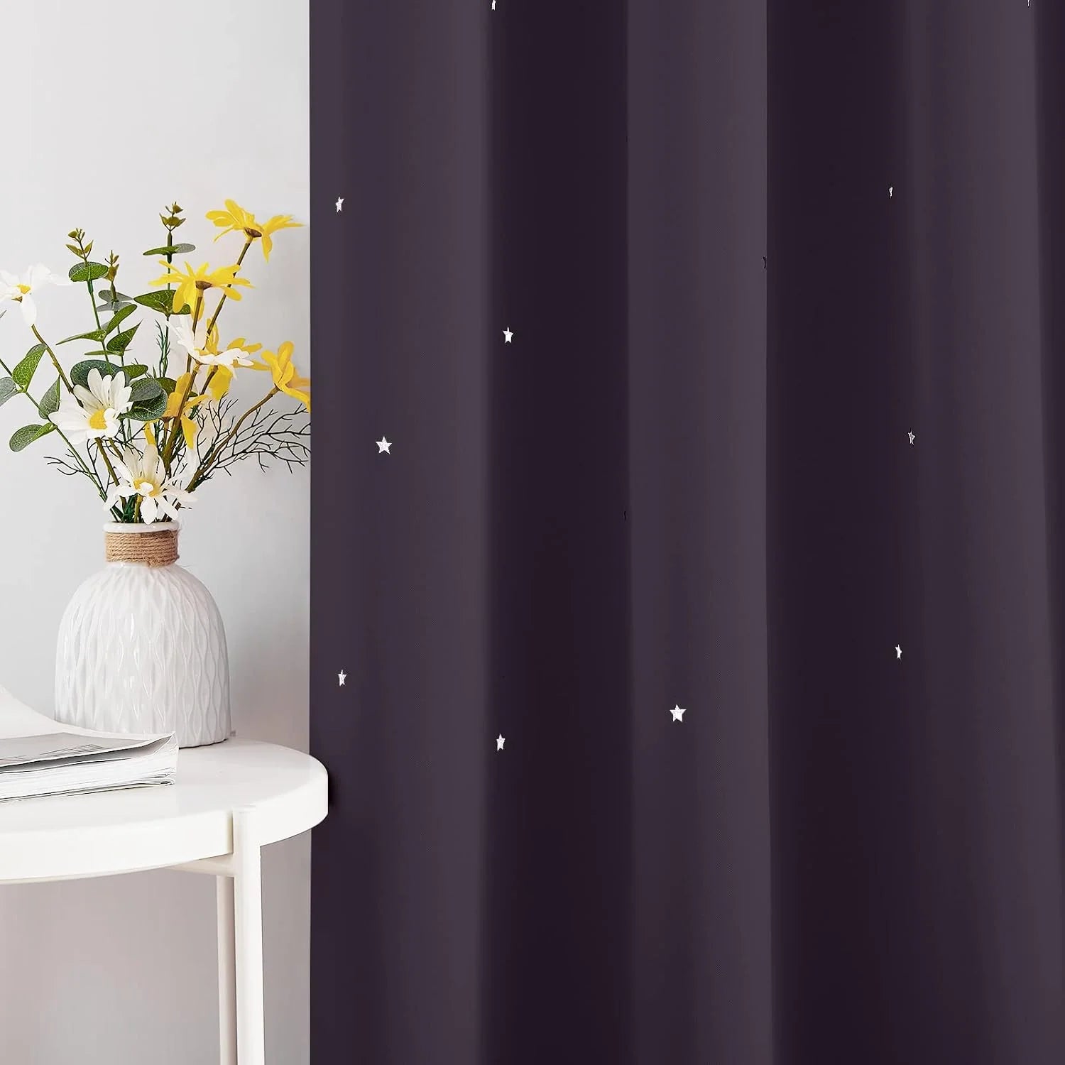 Dark purple curtain with small white star print beside a white table and flower vase