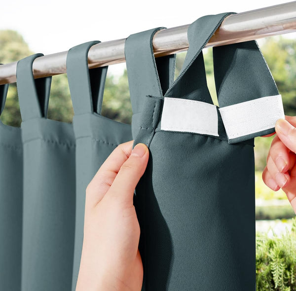 Hands fastening dark teal outdoor curtains with hook and loop tie-top straps on a silver rod.