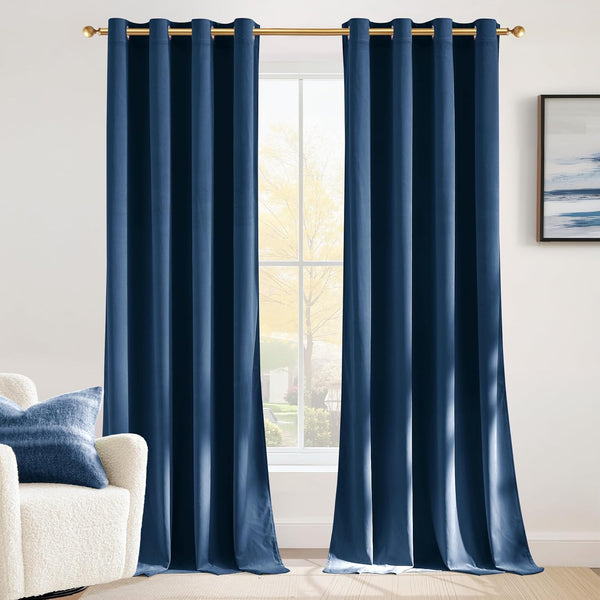 Pair of deep blue velvet window curtains with gold grommet tops on a golden rod in a sunlit room.