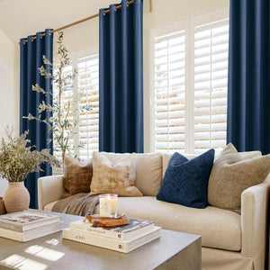 Deep navy blue grommet top curtains hanging on a wooden rod over white window shutters in a cozy living room.