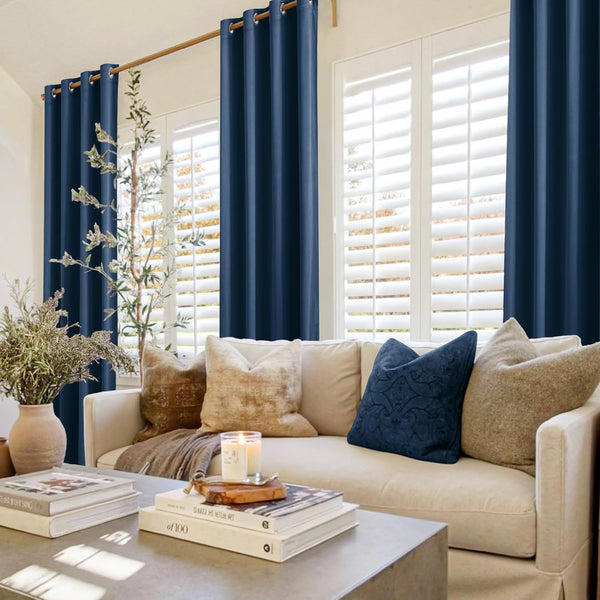 Deep navy blue grommet top curtains hanging on a wooden rod over white window shutters in a cozy living room.