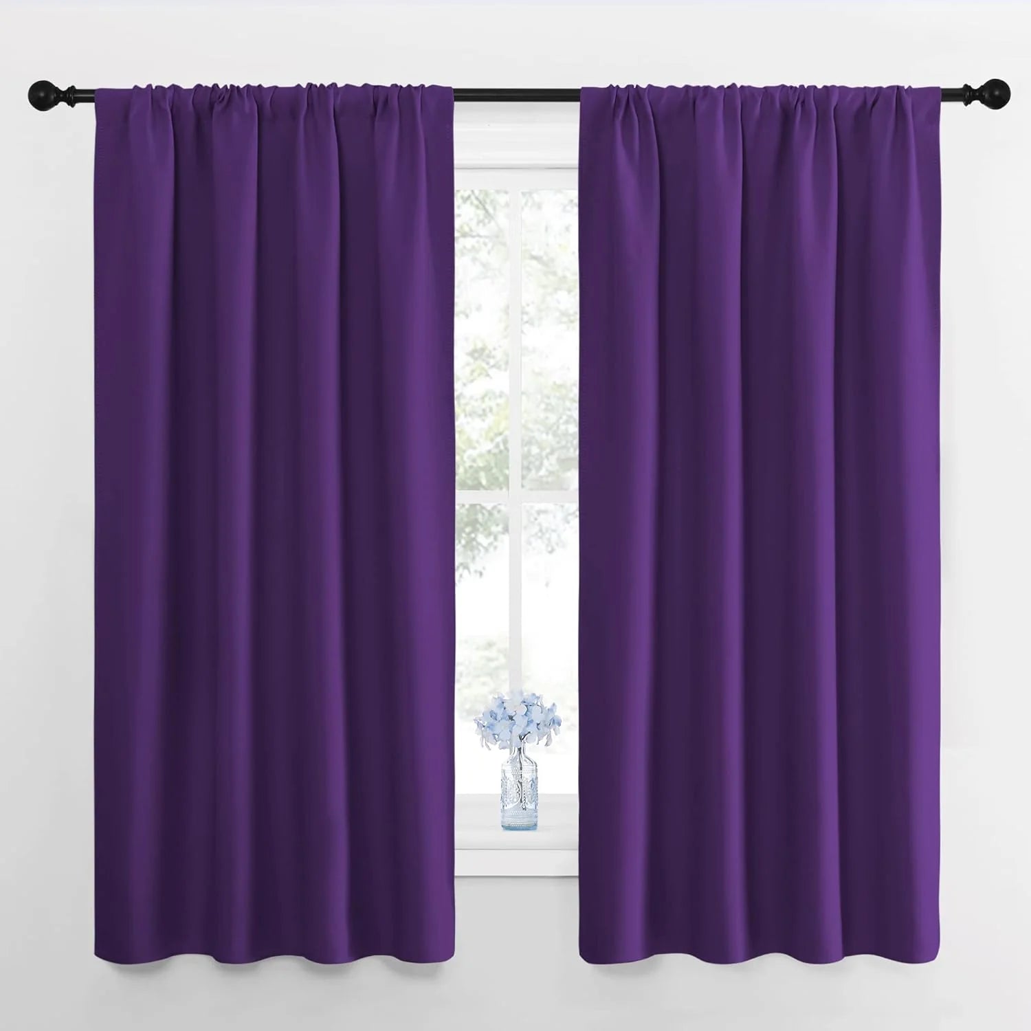 Deep purple opaque curtains with a rod pocket header style on a black curtain rod in a white room.