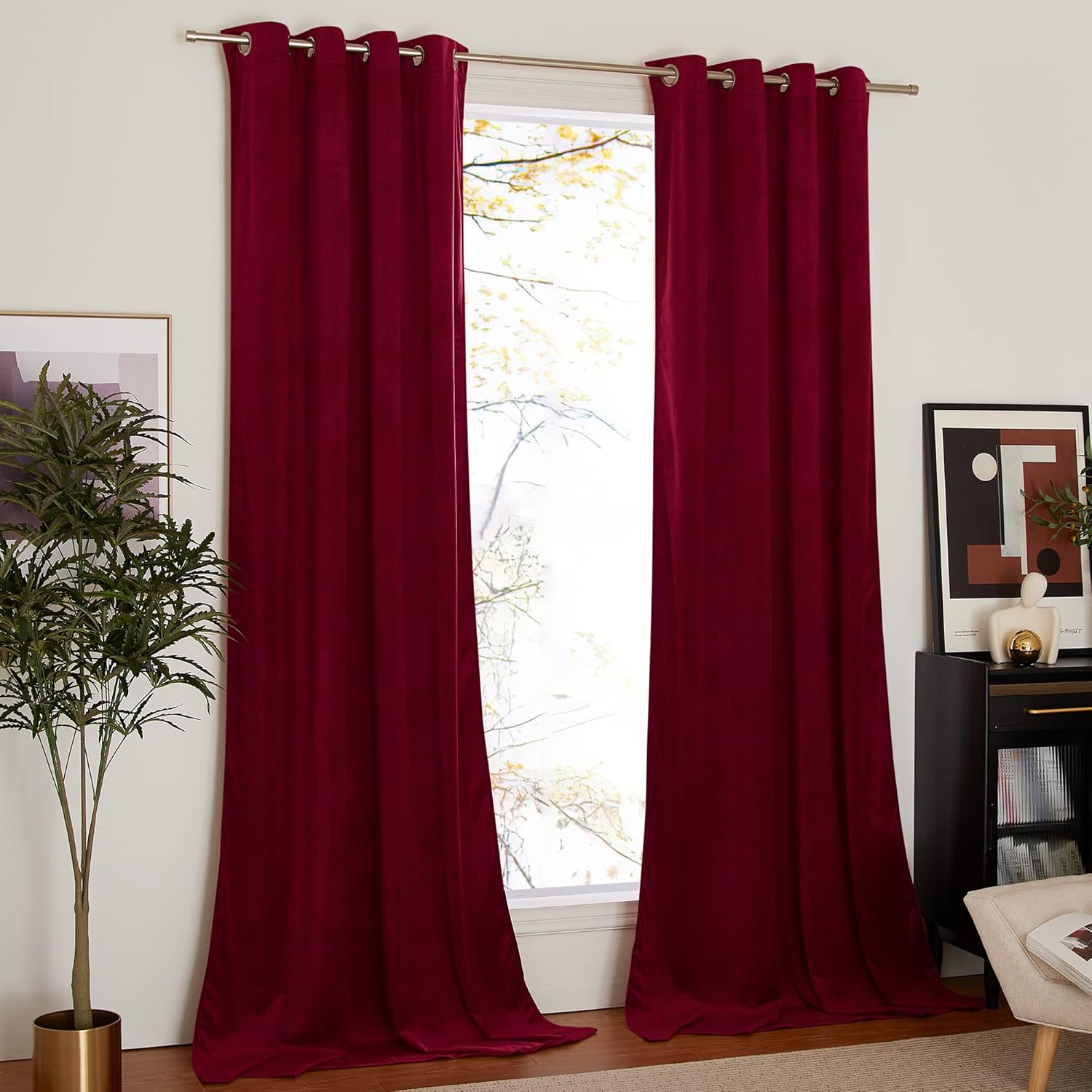 Deep red velvet grommet top blackout curtains hanging on a silver rod in a brightly lit room.