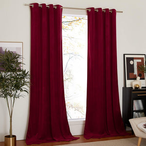 Deep red velvet grommet top blackout curtains hanging on a silver rod in a brightly lit room.
