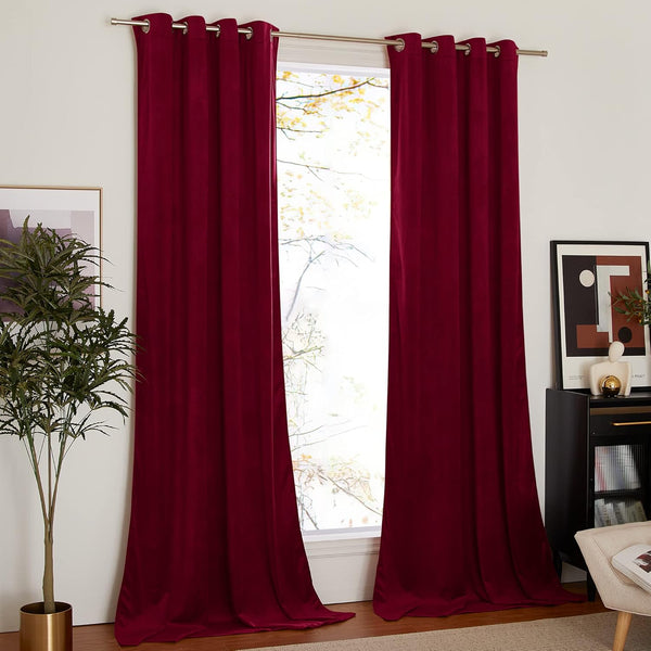 Deep red velvet grommet top blackout curtains hanging on a silver rod in a brightly lit room.