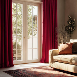 Deep ruby red velvet pleated curtains, floor-to-ceiling, framing bright French doors in a sunlit living room.