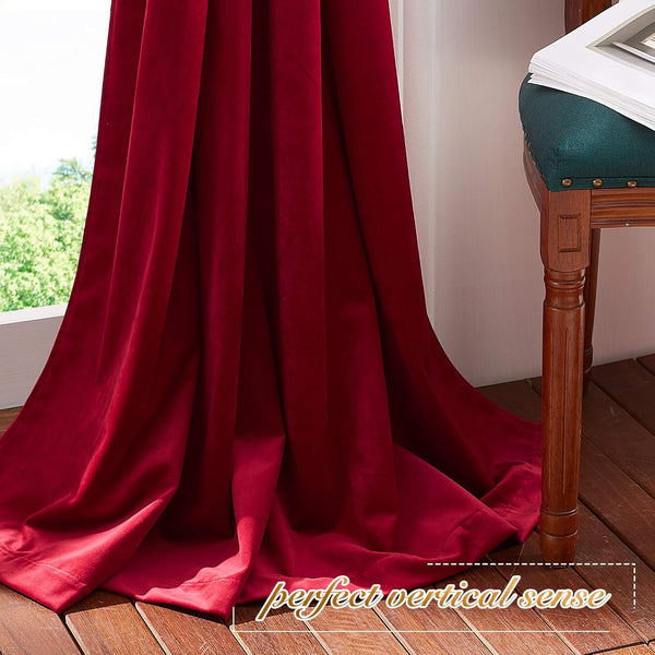 Deep red velvet curtain with rich folds pooling on a wooden floor next to a window, showing luxurious texture.