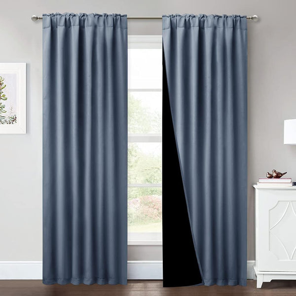 Dusty blue rod pocket blackout curtains hanging in a room, showing the thick black lining.