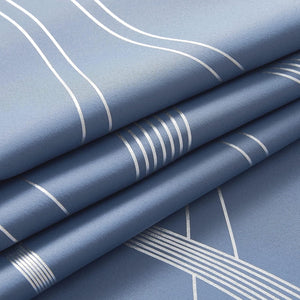 Close-up of dusty blue textile with reflective silver geometric wavy and straight line patterns, folded.