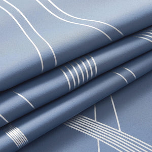 Close-up of a dusty blue fabric with a modern silver geometric line pattern, showing folds.