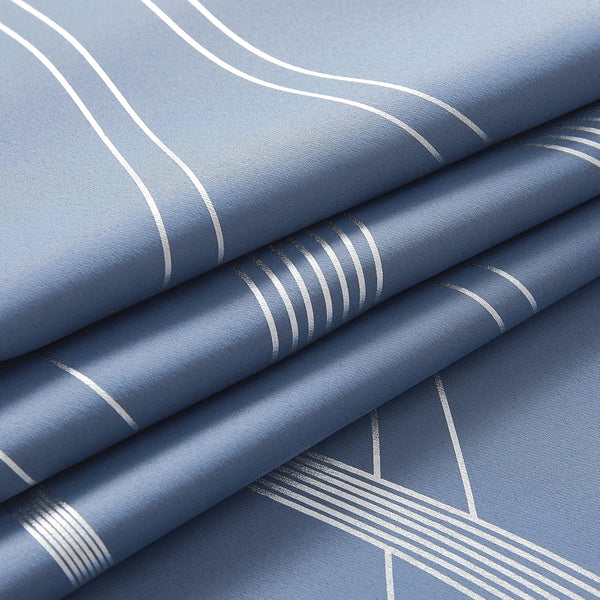 Close-up of a dusty blue fabric with a modern silver geometric line pattern, showing folds.