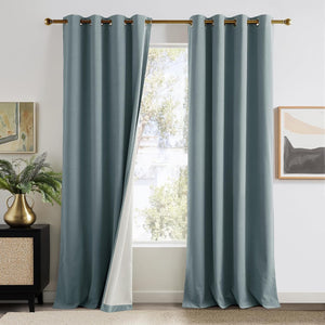 Pair of full-length dusty blue grommet blackout curtains with a visible white lining, hanging on a gold rod.
