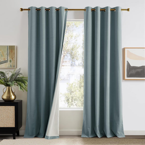 Pair of full-length dusty blue grommet blackout curtains with a visible white lining, hanging on a gold rod.