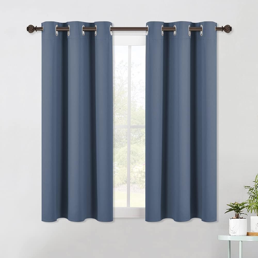 Dusty blue blackout curtain panels with silver grommets on a brown rod over a window.