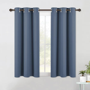 Dusty blue blackout curtain panels with silver grommets on a brown rod over a window.