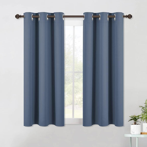 Dusty blue blackout curtain panels with silver grommets on a brown rod over a window.