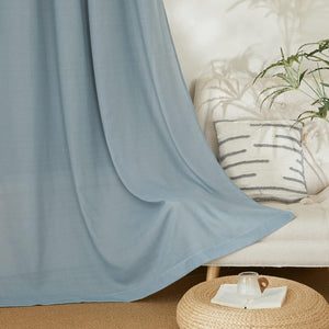 Dusty blue linen blend curtain panel with soft folds in a modern living room. Textured pillow, green plant.